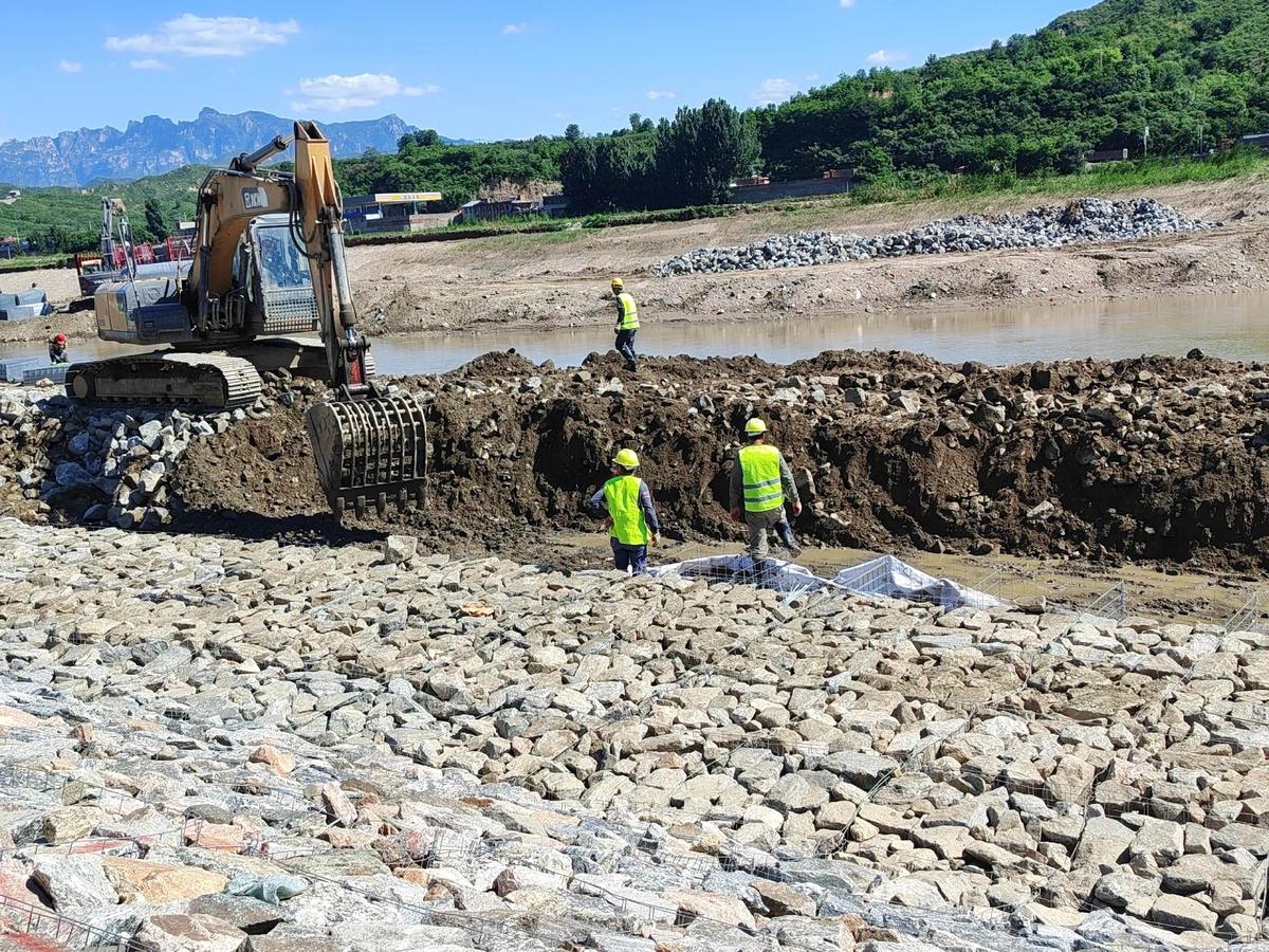 Large-scale gabion construction project with excavator and workers